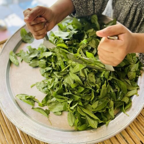 Chopping molokhia leaves with a traditional makhrata on a metal tray
