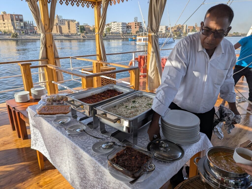 A crew member setting out a buffet on the shaded deck of the dahabeya
