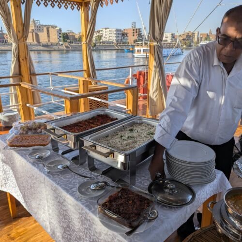 A crew member setting out a buffet on the shaded deck of the dahabeya