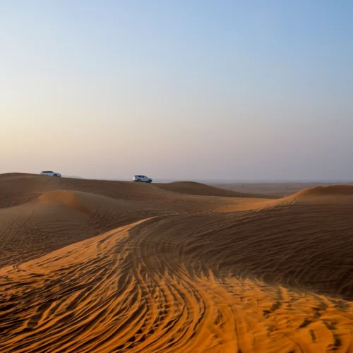 Wind-rippled dunes in the desert near Hurghada, with safari vehicles small on the horizon