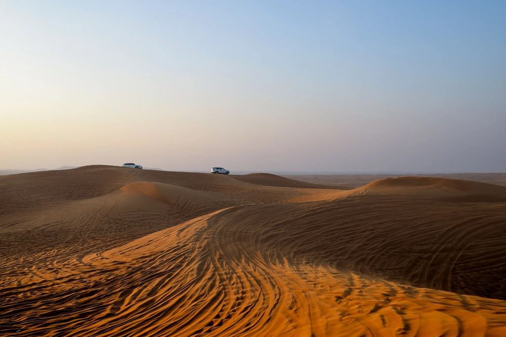Wind-rippled dunes in the desert near Hurghada, with safari vehicles small on the horizon