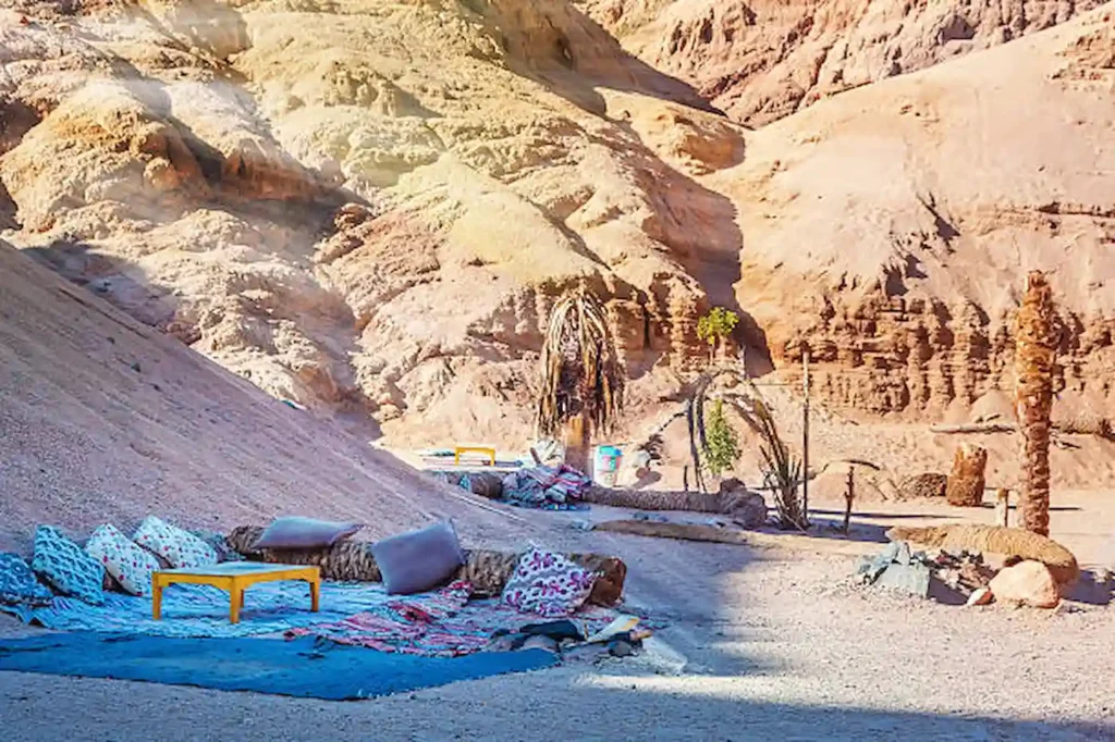 A Bedouin camp with carpets and cushions in the shade of a desert cliff