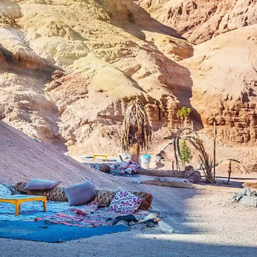A Bedouin camp with carpets and cushions in the shade of a desert cliff