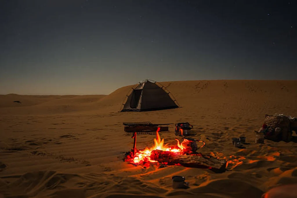 A campfire burning beside a tent in the desert at night