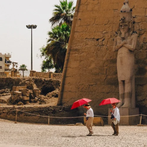 The entrance pylon of Luxor Temple with the seated colossus of Ramesses II and two visitors under red parasols