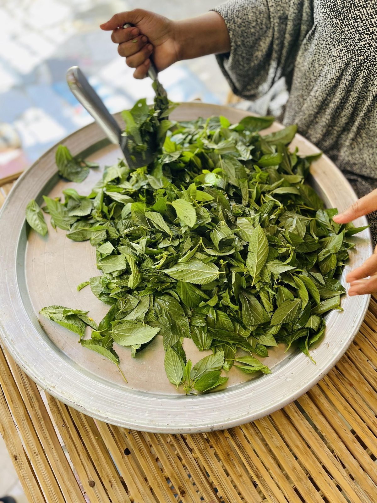 Fresh molokhia leaves being chopped with a makhrata on a round tray - traditional Egyptian cooking