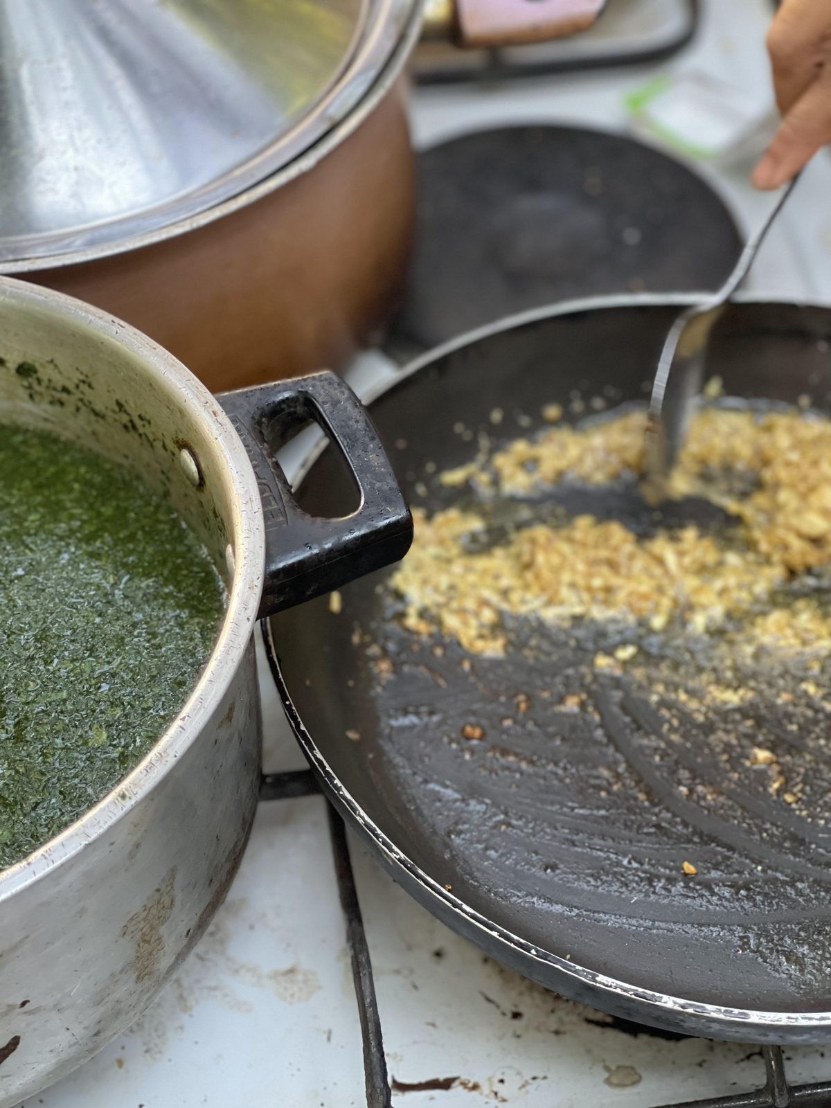 Green molokhia soup in the pot next to the ta'leya pan with fried garlic - the last step of the preparation