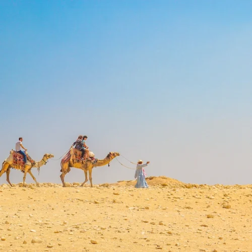 Two camel riders crossing pale desert sand under a wide blue sky in Egypt