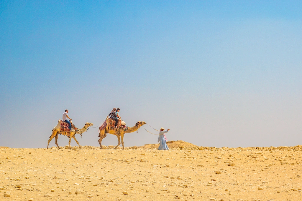 Two camel riders crossing pale desert sand under a wide blue sky in Egypt