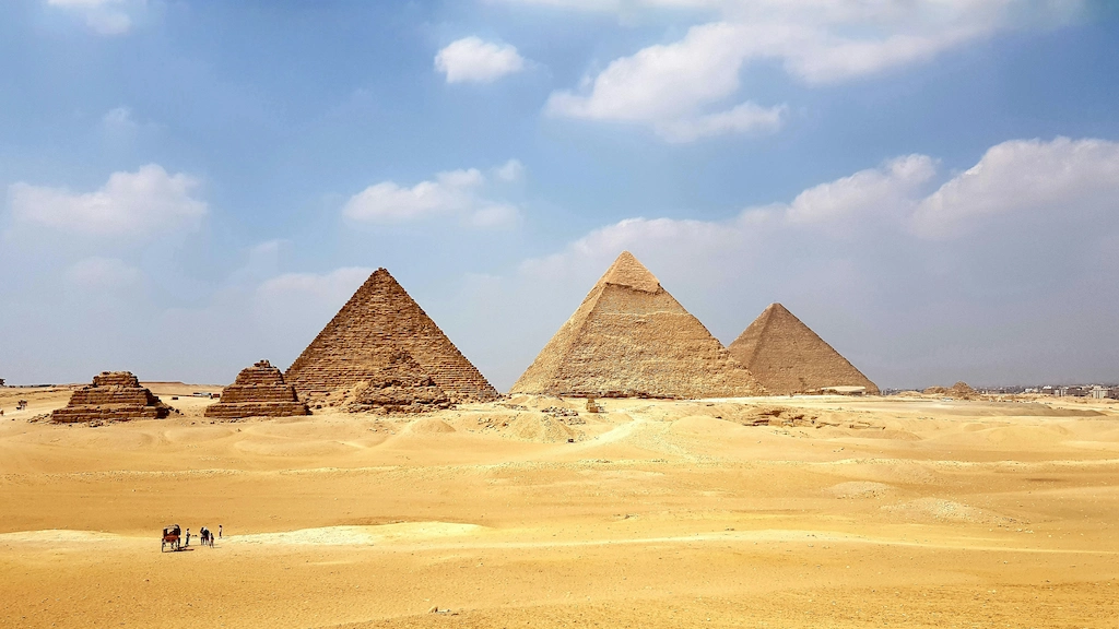 The three pyramids of Giza rising from the sand under a blue sky with scattered cloud