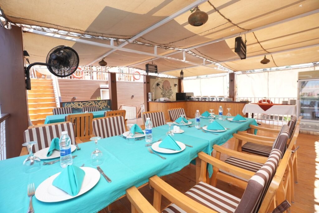 A long table laid for dinner under the deck awning of a dahabeya, turquoise cloth and folded napkins