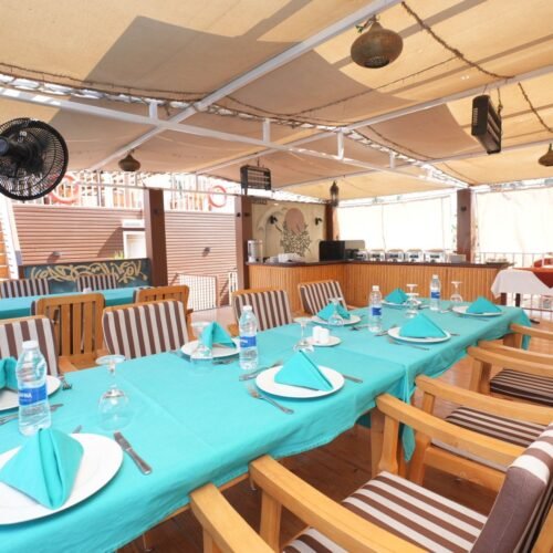 A long table laid for dinner under the deck awning of a dahabeya, turquoise cloth and folded napkins