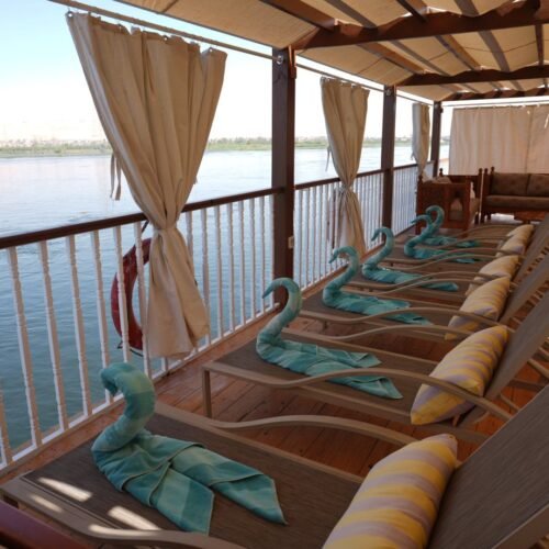 Sun loungers under a wooden pergola on the upper deck of a Nile dahabeya, the river and the west bank beyond